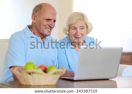 Two smiling people, active senior couple, eating fruits and enjoying modern technology using laptop computer with wireless internet at home