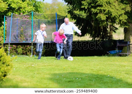 Happy family of three, healthy grandfather with laughing grandsons, twin teenage boys, playing soccer in the garden at the backyard of the house on sunny summer vacation day