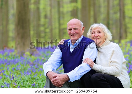 Mature family, healthy caring senior couple, hiking in beautiful spring forest, enjoying nature and blooming bluebells or wild hyacinth flowers - active retirement concept