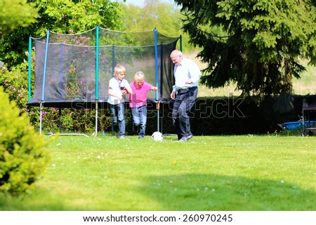 Happy family of three, healthy grandfather with laughing grandsons, twin teenage boys, playing soccer in the garden at the backyard of the house on sunny summer vacation day