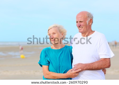 Loving amusing elderly couple enjoying the beach and sea breeze on sunny day - active healthy retirement concept