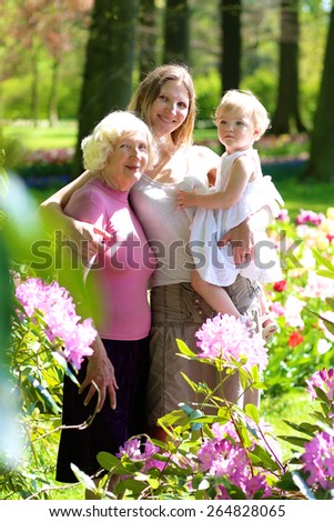 A happy family of three generations, mother, daughter, grandmother and little toddler granddaughter are enjoying together beautiful blossoming floral park on a sunny spring or summer day