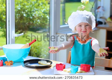 Little happy child, adorable toddler girl in white chef hat helping mother cooking delicious pasty in the kitchen