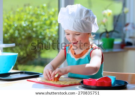 Little happy child, adorable toddler girl in white chef hat helping mother cooking delicious pasty in the kitchen