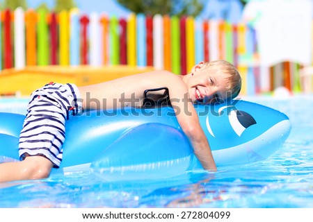 Happy kid, blonde caucasian boy, having fun floating and sliding in water park on inflatable dolphin toy enjoying sunny summer vacations in tropical resort