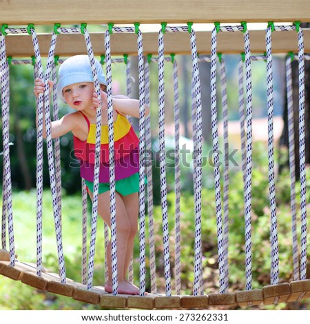 Funny little child, blond sportive toddler girl wearing colorful swimming suit, having fun climbing on playground in the park on a sunny summer day at vacation holidays resort