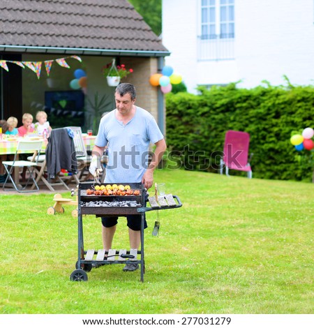 People enjoying summertime. A man cooking meat on barbecue for summer family dinner at the backyard of the house.