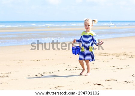 Cute active child playing on sandy beach. Happy little girl enjoying summer holidays on a sunny day. Family with young kids on vacation at the North Sea coast.