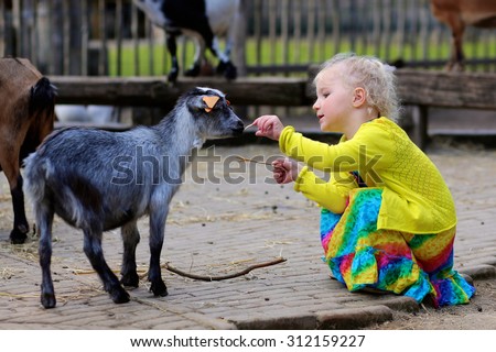 Toddler girl petting little goat in the kids farm. Cute kind child feeding animals in the zoo.