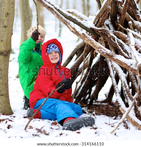 Happy children playing in winter forest. Kids enjoying snow building tent from trees branches. Healthy teenage boys having active snowy holidays.