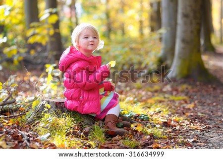 Cute little girl wearing warm pink jacket playing in beautiful autumn forest on sunny fall day