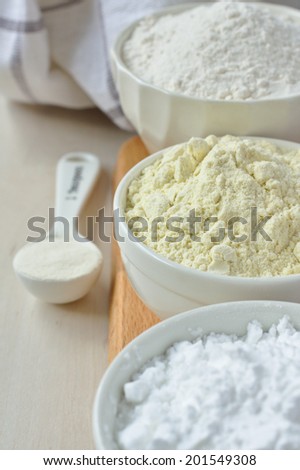 Three bowls with gluten free flour - rice flour, millet flour and potato starch and spoon with xanthan gum