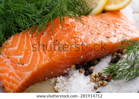 Delicious salmon fillet, rich in omega 3 oil, aromatic spices and lemon on vintage cutting board on black wooden background. Healthy food, diet and cooking concept.