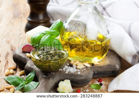 Homemade green pesto in glass bawl on a rustic wooden cutting board and fresh ingredients. Selective focus.