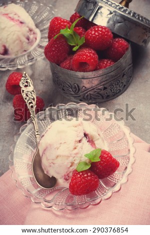 Delicious berry ice cream on glass plate decorated with fresh raspberries on vintage gray background.  Selective focus. Retro style toned.  Party concept.