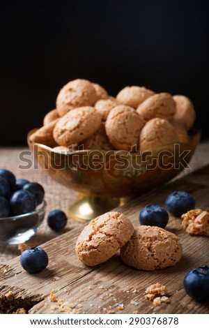 Italian almond cookie amaretti with blueberries on rustic wooden board, selective focus, law key.