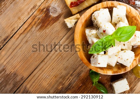 Cubes of feta cheese in olive wood bowl and green and black olives on rustic wooden background.  Selective focus. Food background with copy space.