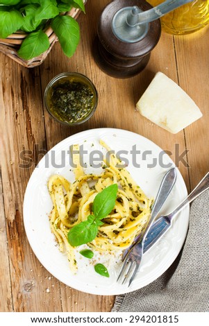 Cooked homemade tagliatelle pasta with green pesto sauce, grated pecorino cheese and basil on white plate on old wooden background.  Top view.