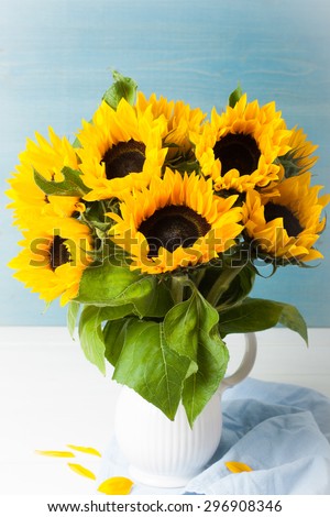 Still life with beautiful sunflowers bouquet in white vase on blue wooden background. Greeting card concept.