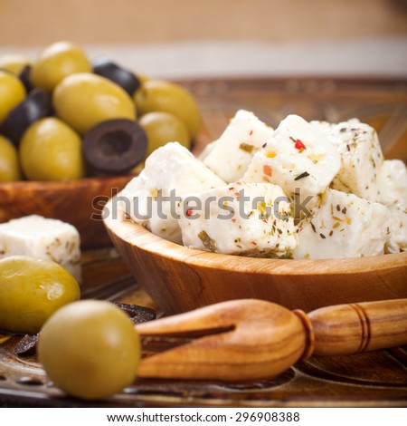 Cubed feta cheese in olive wood bowl and green and black olives on rustic wooden background.  Selective focus.