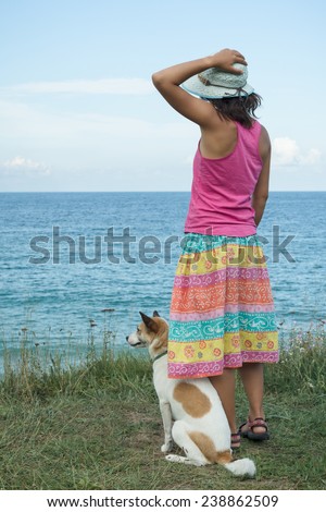 Young woman and her dog watching the sea and relaxing on a cliff