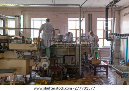 NIZHNY TAGIL, RUSSIA - APRIL 24, 2015: Maintenance of automatic production line of ice cream. Man repairing feeding formula. Women are laid wooden popsicle sticks