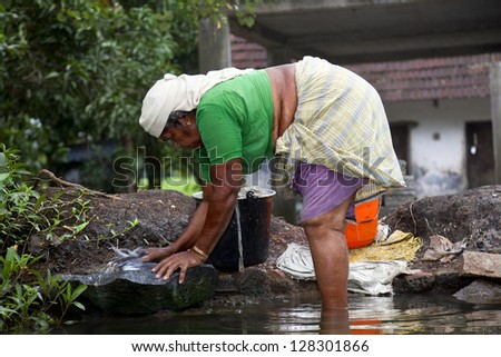 ALLEPY-SEPTEMBER 2012: An Indian woman washes her clothes on a rock in one of the canals around Alappuzha on september 7, 2012 in Allepy, India.
