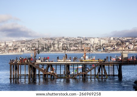 VALPARAISO-APRIL 3,2015: Some people fishing off the side of the pier in Valparaiso, face the downtown cityscape across Valparaiso Bay on april 3, 2015 in Chile