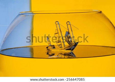 glass toy ship in water on color background