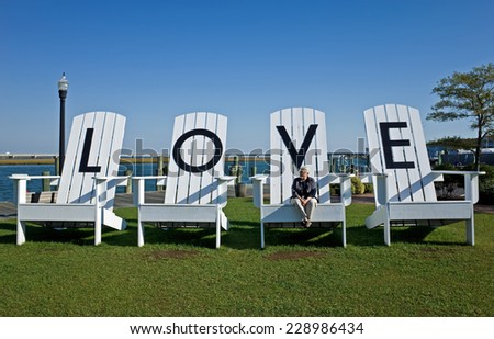 Woman sitting on a giant lawn chair in a public park inscribed with letters spelling LOVE.