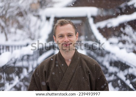 Western man smiling wearing Japanese Yukata during winter snow on old wooden bridge