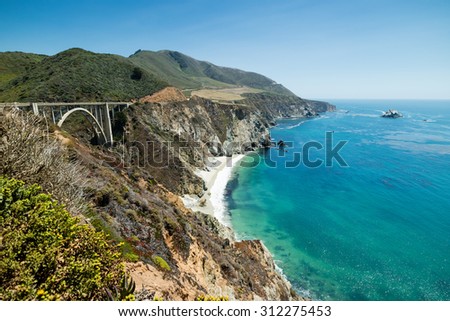 Beautiful view of Brixby bridge and the Big Sur on the Pacific Coast Highway Route 1 in California state, USA. Stunning blue water and green mountain cliffs surround paradise beach