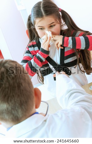A sweet little girl sneezing into a tissue while her pediatrician sits and looks on worriedly