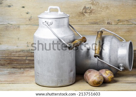 Two potatoes and aluminum old milk cans on a wooden background