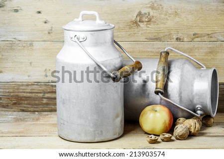 An apple, walnuts and aluminum old milk cans on a wooden background
