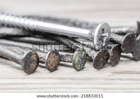 The leadership concept - The new steel wood screw over group of old rust nails on a wooden background