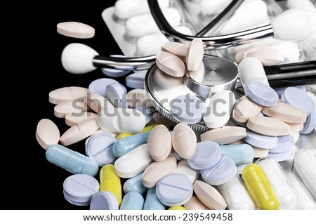 Close-up of phonendoscope, medicine color tablets and white capsules in the blister on a black background