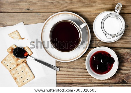 Close-up of a cup of tea, milk, some dry loaves and strawberry jam on a  wooden background in the horizontal format