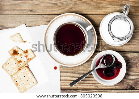 Close-up of a cup of tea, milk, some dry loaves and strawberry jam on a  wooden background in the horizontal format