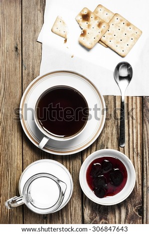 Close-up of a cup of tea, milk, some dry loaves and strawberry jam on a  wooden background in the vertical format