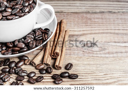 Close-up of coffee beans, cinnamon sticks and a cup on a wooden background