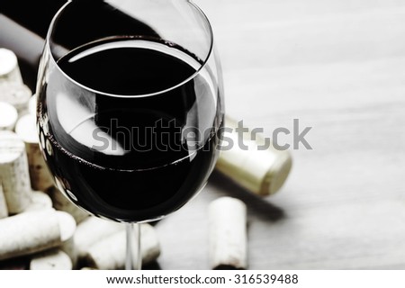 Close-up of a red wine glass, corks and a bottle of wine on a wooden background