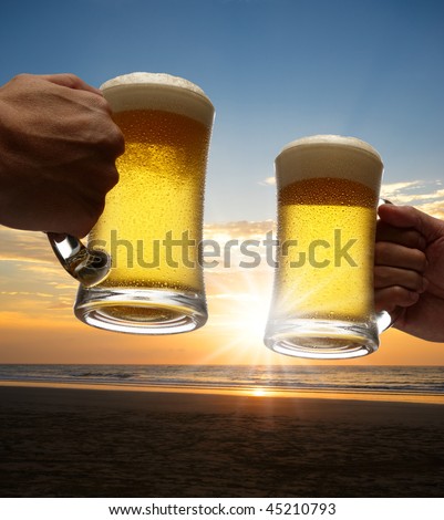 hands holding beers toasting on beach at sunset