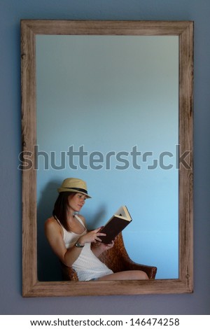 Young woman reading a book in front of a mirror of an old house in Begur, Costa Brava, Catalonia, Spain