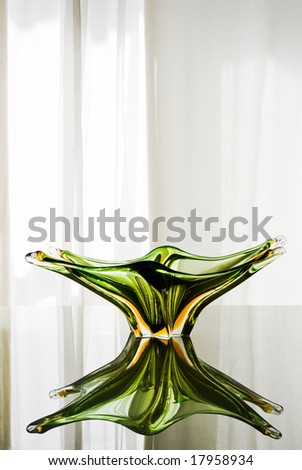 Precious green Murano glass plate on a green glass table. Soft light behind the white curtain on the back. Amazing sharp reflections.