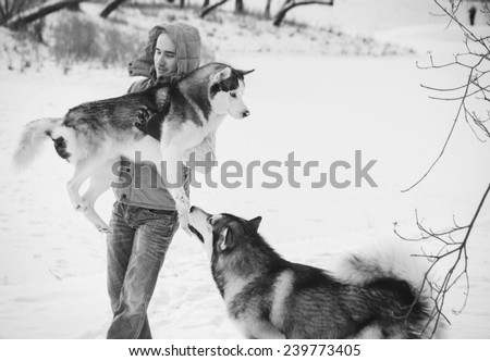 Man walking with dog winter time with snow in forest Malamute and Huskies friendship black and white