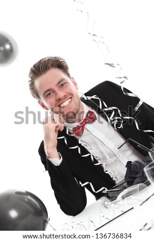 Happy party guy. Wearing a black suit and bowtie. Balloons in the background. White background.