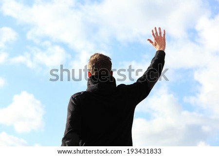 A silhouette of a young man wearing a black hoodie standing in front of a blue cloudy sky.