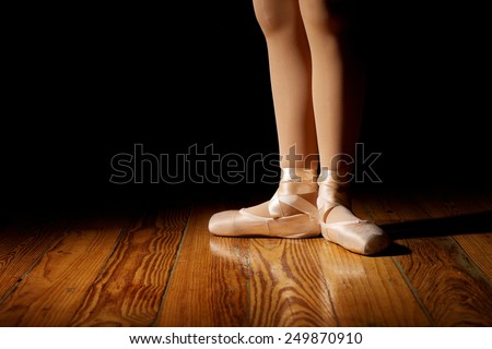 Closeup of a ballerina\'s feet in pointe shoes on a vintage, wood floor with black background. First position, flat footed in pointe shoes.
