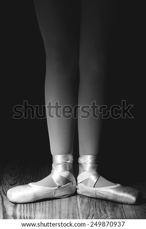 Closeup of a ballerina\'s feet in pointe shoes on a vintage, wood floor with black background. First position, flat footed in pointe shoes. Black and white image